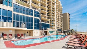 A hotel pool area with a large pool, sun loungers, and a building with multiple balconies. - Phoenix III by Southern Vacation Rentals (Orange Beach)
