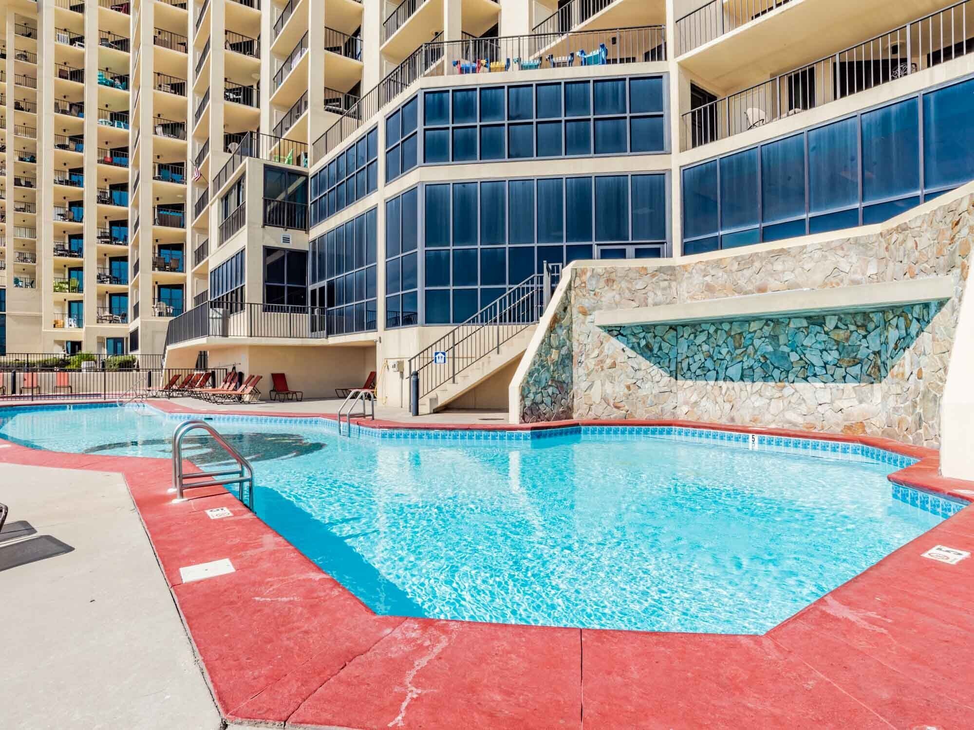 Ein mehrstöckiges Hotel mit Swimmingpool, Balkonen und einer Steinmauer.