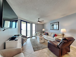 Relax in this cozy living space with a flat-screen TV, ceiling fan, and large window.