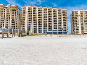A beachfront high-rise hotel with multiple balconies, a sandy beach in the foreground, and a clear blue sky. - Phoenix III by Southern Vacation Rentals (Orange Beach)