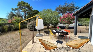 Un patio esterno con un tavolo apparecchiato per mangiare, circondato da sedie in vimini, una lampada gialla e un'area salotto coperta.