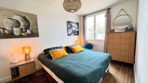 Um quarto com cama, luminárias de cabeceira, cômoda, espelho e obras de arte na parede.