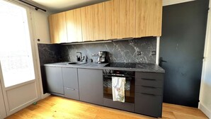 Una cucina compatta con mobili scuri, un piano di lavoro nero, forno integrato e macchina da caffè.