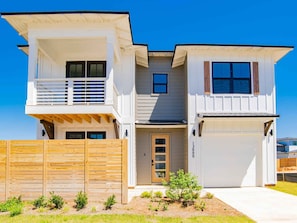 Stylish two-story home with a central entrance and garage doors, set amidst a beautifully landscaped garden.