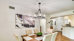 Een eetgedeelte met een houten tafel, beige stoelen en een kroonluchter. Drie ingelijste kunstwerken hangen aan de muur.