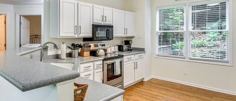 Una cocina moderna con armarios blancos, estufa de acero inoxidable y ventana con persianas.