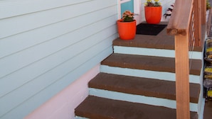 A house with light blue siding, a wooden front porch, and two potted plants on the steps.