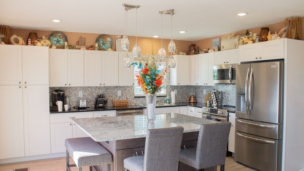 A modern kitchen with white cabinets, a marble island, and stainless steel appliances.