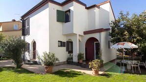 Un edificio a due piani con facciata bianca, dettagli rossi e un piccolo patio con posti a sedere all'aperto.
