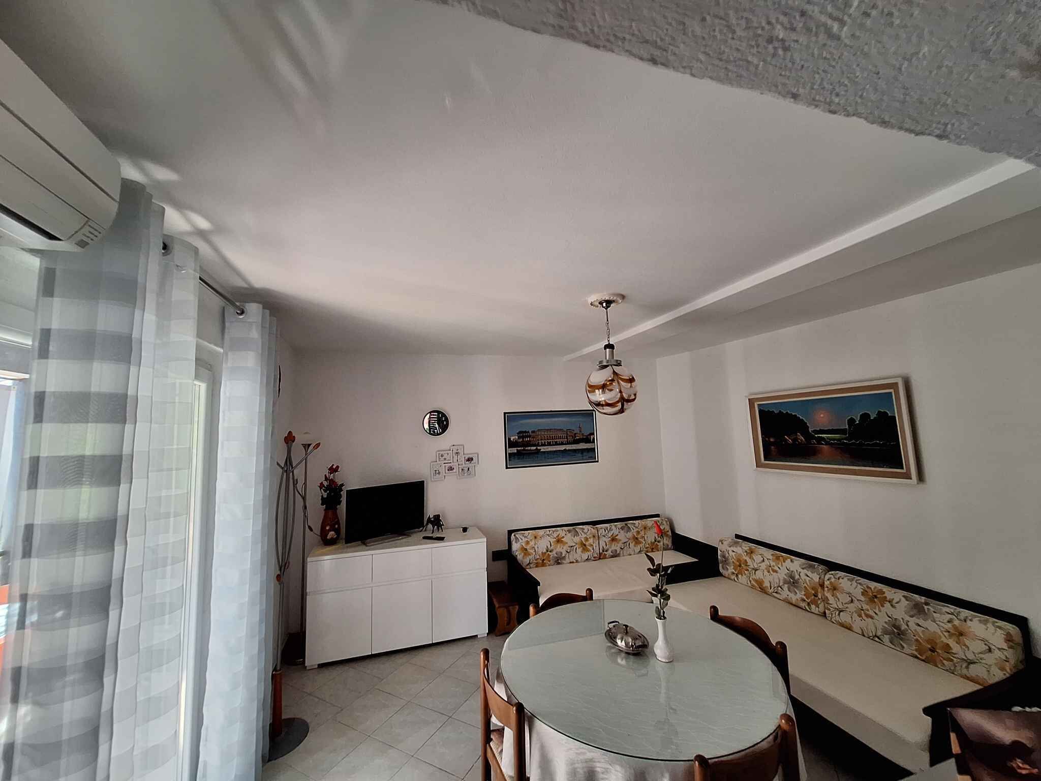 Un coin repas avec une table ronde, un canapé, un téléviseur posé sur un meuble blanc et un luminaire au plafond.
