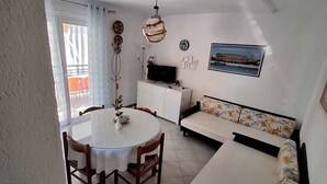 Un ambiente compatto con angolo pranzo, divano, televisore e ventilatore a soffitto.