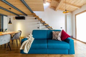 A modern living room with a blue sofa, a wooden staircase, and a dining area with a table and chairs.