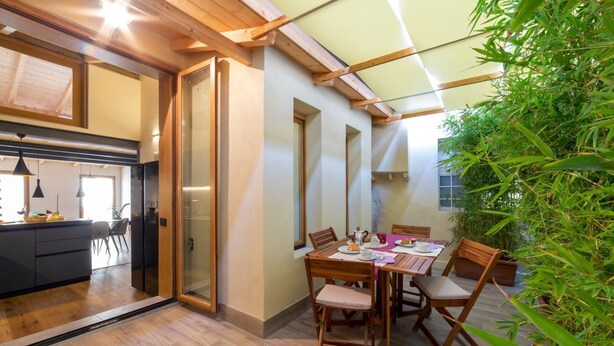 A dining area with a table and chairs, a kitchen in the background, and a large window. - Industrial design loft with outdoor living terrace (Florence)
