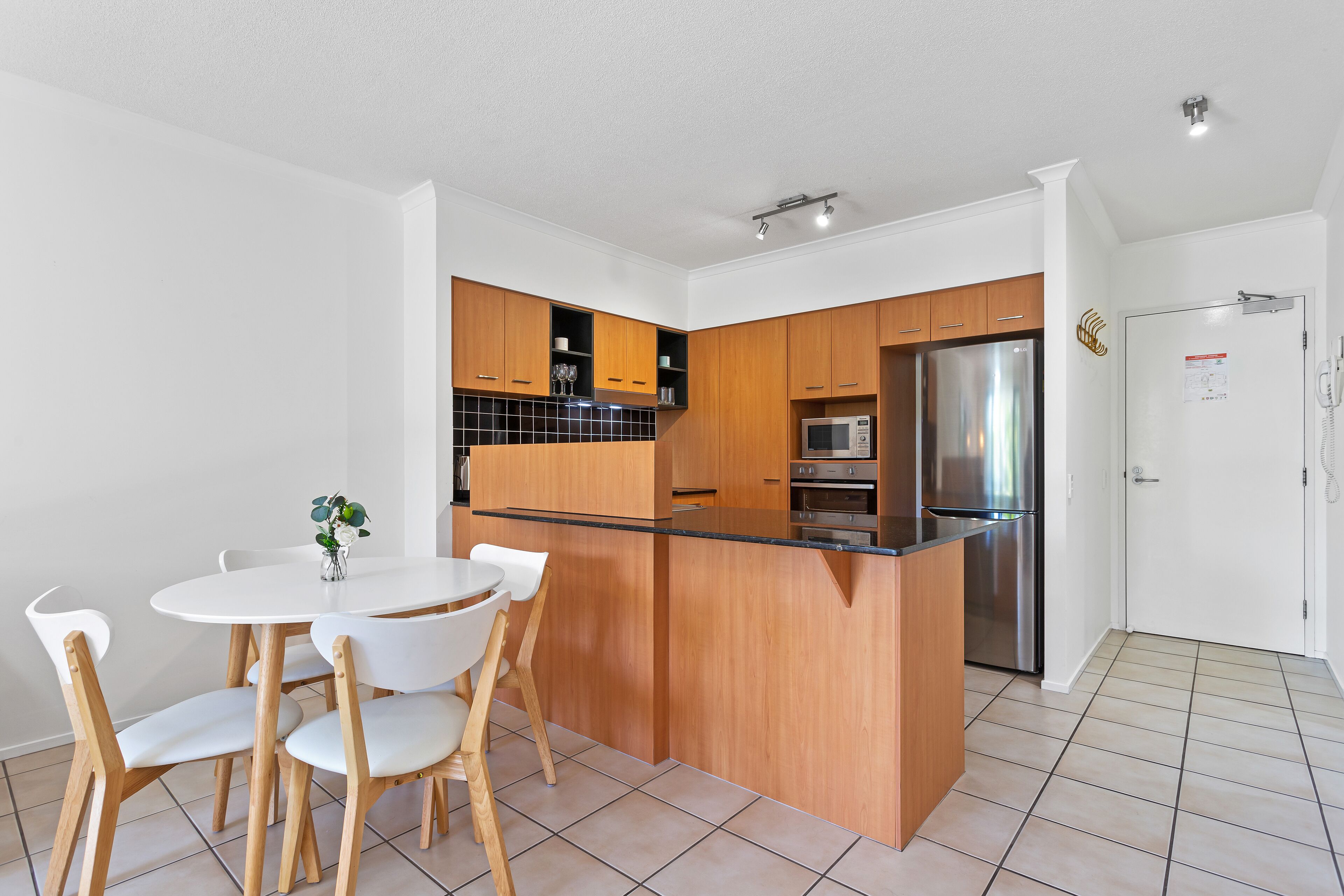 A modern kitchen with wooden cabinets, a stainless steel refrigerator, and a black countertop.