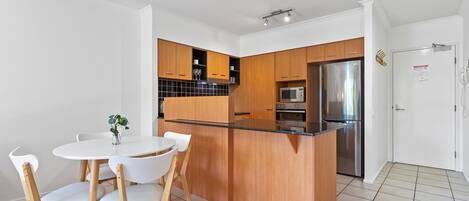 A modern kitchen with wooden cabinets, a stainless steel refrigerator, and a black countertop.