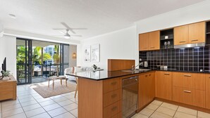 A modern kitchen with wooden cabinets, a black backsplash, and a central island. - Seaforth Resort (Alexandra Headland)