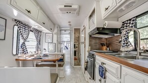 A compact RV kitchen with white cabinetry, a wooden countertop, and a window with checkered curtains. - River Access, 20% Off, Glamping, Couple, Nature (New Braunfels)