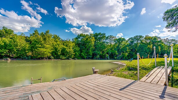 A wooden dock extending into a calm river, surrounded by lush greenery and trees. - River Access, 20% Off, Glamping, Couple, Nature (New Braunfels)