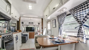 A compact RV kitchen with a stove, sink, and dining area. - River Access, 20% Off, Glamping, Couple, Nature (New Braunfels)
