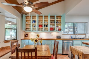 A kitchen with teal cabinets, a wooden dining table, and a ceiling fan.