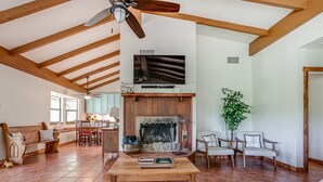 A spacious living room with a fireplace, wooden beams, a dining area, and a TV mounted on the wall. - Ask for 20% Off, Cozy Home, Riverfront, Nature (New Braunfels)
