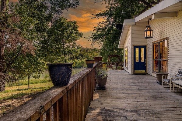 A wooden deck with potted plants, a blue door, and a hanging lantern.