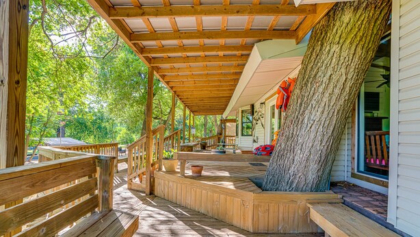 A wooden deck with a covered area, a large tree trunk, and a house with a porch. - Ask for 20% Off, Cozy Home, Riverfront, Nature (New Braunfels)