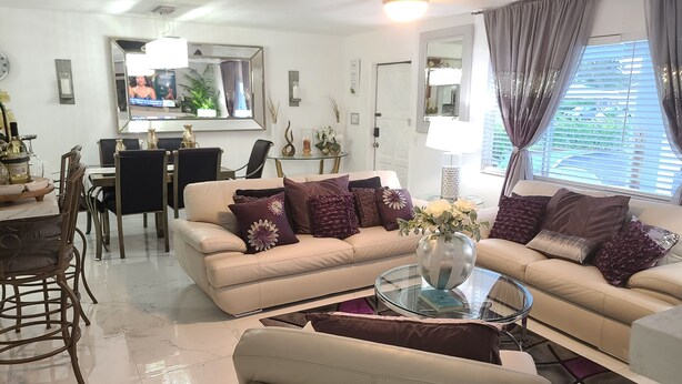 A modern living room with a beige sofa set, a glass coffee table, and a dining area with a glass table and chairs.