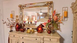 A room with a large ornate mirror, a cream-colored dresser with decorative vases, and a bed with red bedding.