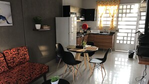 Una sala de estar moderna con un sofá, una mesa de comedor con sillas, una zona de cocina con un refrigerador y un ventanal con cortinas.