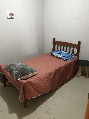 A single bed with a wooden headboard, a red bedspread, and a grey pillow. A small black table is beside the bed. - Fully equipped apartment in the southern part of the city (San Pedro Tlaquepaque)
