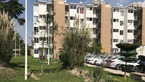 Un edificio residencial con balcones numerados, una zona de estacionamiento y una farola.