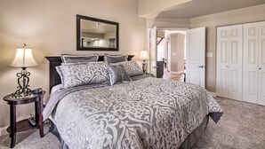 A bedroom with a large bed, two bedside tables with lamps, a mirror above the bed, and a closet with three doors. - Cozy + Deluxe Branson Condo w/ Covered Balcony (Branson)