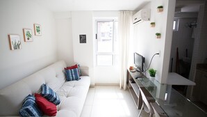 A modern living room with a sofa, a glass coffee table, and a TV. There are potted plants on the wall and a door leading to another room. - Carpediem - Apart beira mar Cabo Branco (João Pessoa)