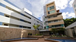 A multi-story building with a courtyard featuring a swimming pool, outdoor seating, and a small palm tree. - Carpediem - Apart beira mar Cabo Branco (João Pessoa)