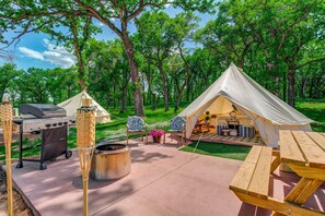Un camping con una tienda de campaña, una parrilla y asientos al aire libre.