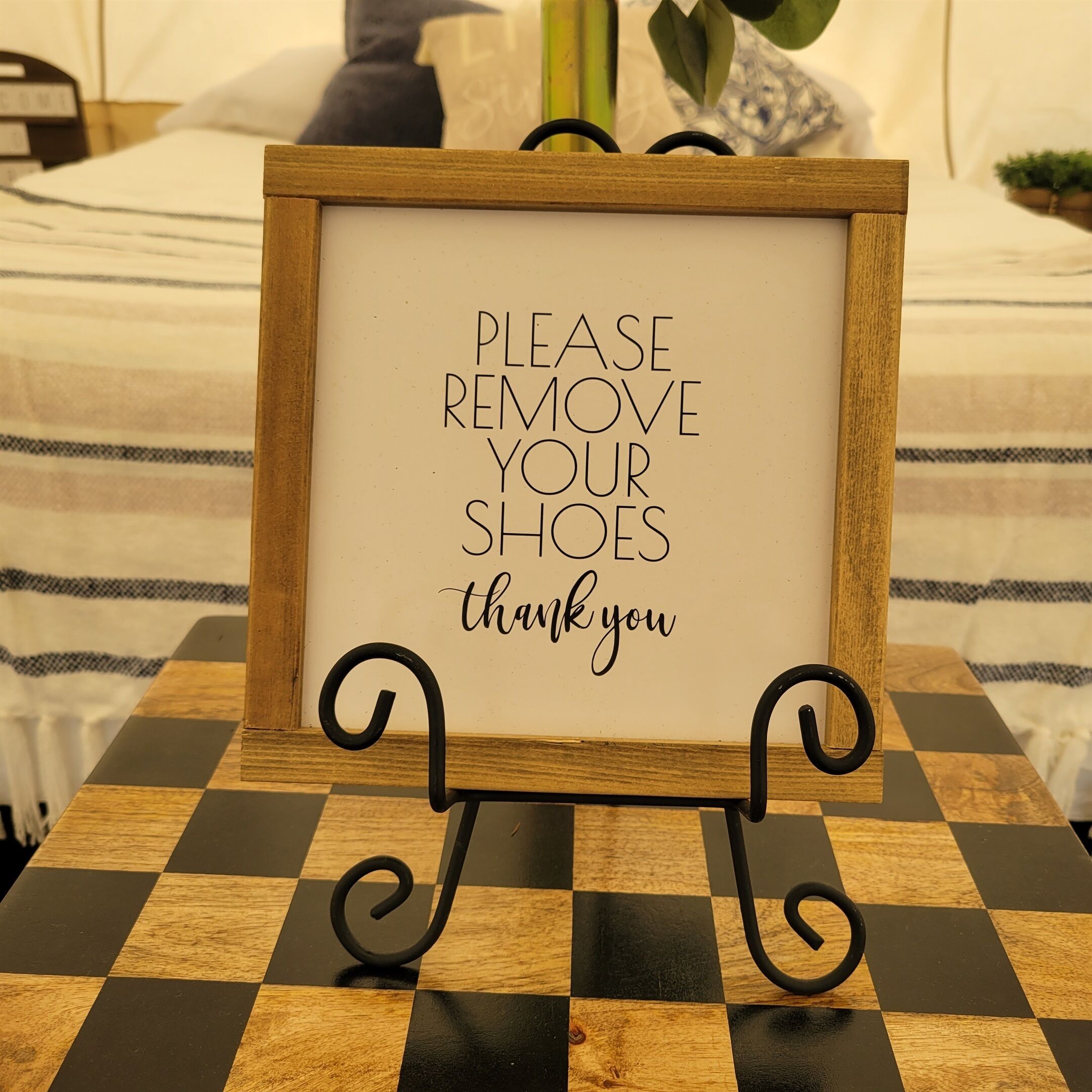 A framed sign with the text "PLEASE REMOVE YOUR SHOES thank you" on a checkered table.