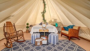 Interior de una carpa con una cama, dos mecedoras, una mesita y un letrero de bienvenida.