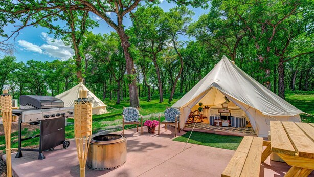 Un camping con una tienda de campaña, una parrilla y asientos al aire libre.