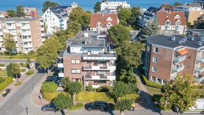 Ein Wohngebiet mit modernen Mehrfamilienhäusern, einer Straße mit parkenden Autos und Blick auf das Meer.