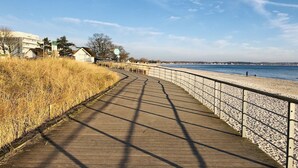 Ein hölzerner Steg verläuft entlang eines Strandes, gesäumt von einem Metallgeländer, und führt zu einem sandigen Ufer.
