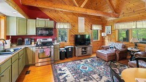 Interior acogedor de una cabaña con vigas de madera, una cocina con estufa y microondas, un televisor, una chimenea y una alfombra grande.