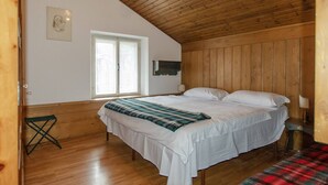 A bedroom with a wooden ceiling, a bed with white bedding, a window, and a small table with a lamp. - Spazioso appartamento centralissimo con wi-fi. (Cortina d´Ampezzo)
