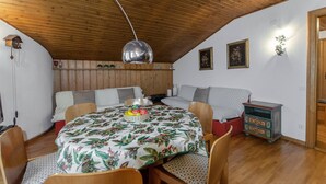 A cozy room with a wooden ceiling, a round table with a floral tablecloth, a bench, and a small cabinet. - Spazioso appartamento centralissimo con wi-fi. (Cortina d´Ampezzo)