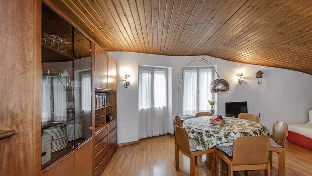 A dining area with a wooden ceiling, a round table with chairs, a television, and a bookshelf with glassware. - Spazioso appartamento centralissimo con wi-fi. (Cortina d´Ampezzo)