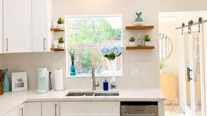 Une cuisine moderne avec des meubles blancs, un lave-vaisselle en acier inoxydable, un ventilateur de plafond et une fenêtre donnant sur un paysage verdoyant.