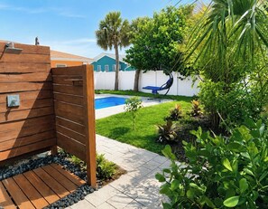 A wooden deck with a pool, surrounded by greenery and a white fence.
