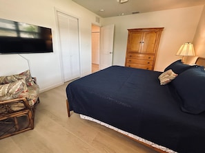 A bedroom with a bed, a television mounted on the wall, a wooden wardrobe, and a chair with a patterned cushion.