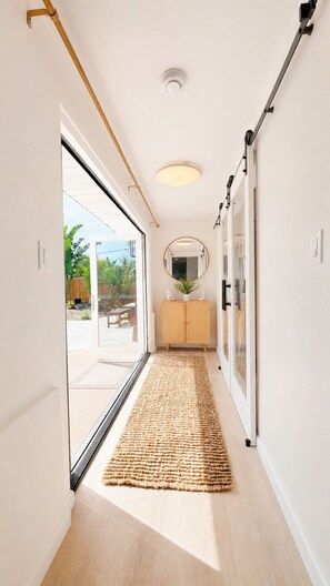 Un couloir doté d’un plancher en bois, d’un tapis tissé, d’une armoire en bois et d’un miroir rond accroché au mur.