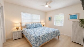 A bedroom with a bed, two bedside tables, a ceiling fan, and a window with blinds.